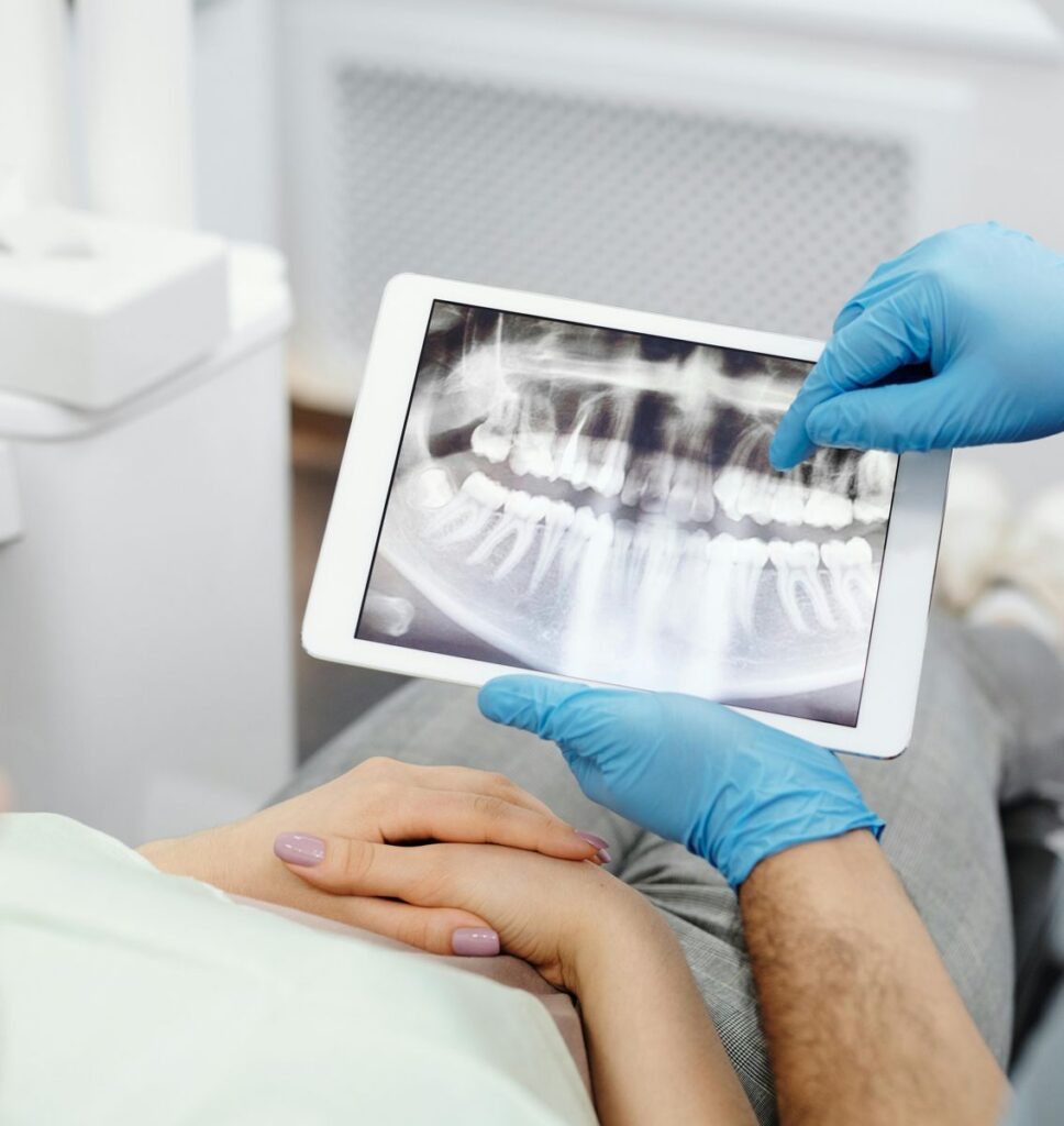Dentist pointing to a dental X-ray on a tablet during an exam